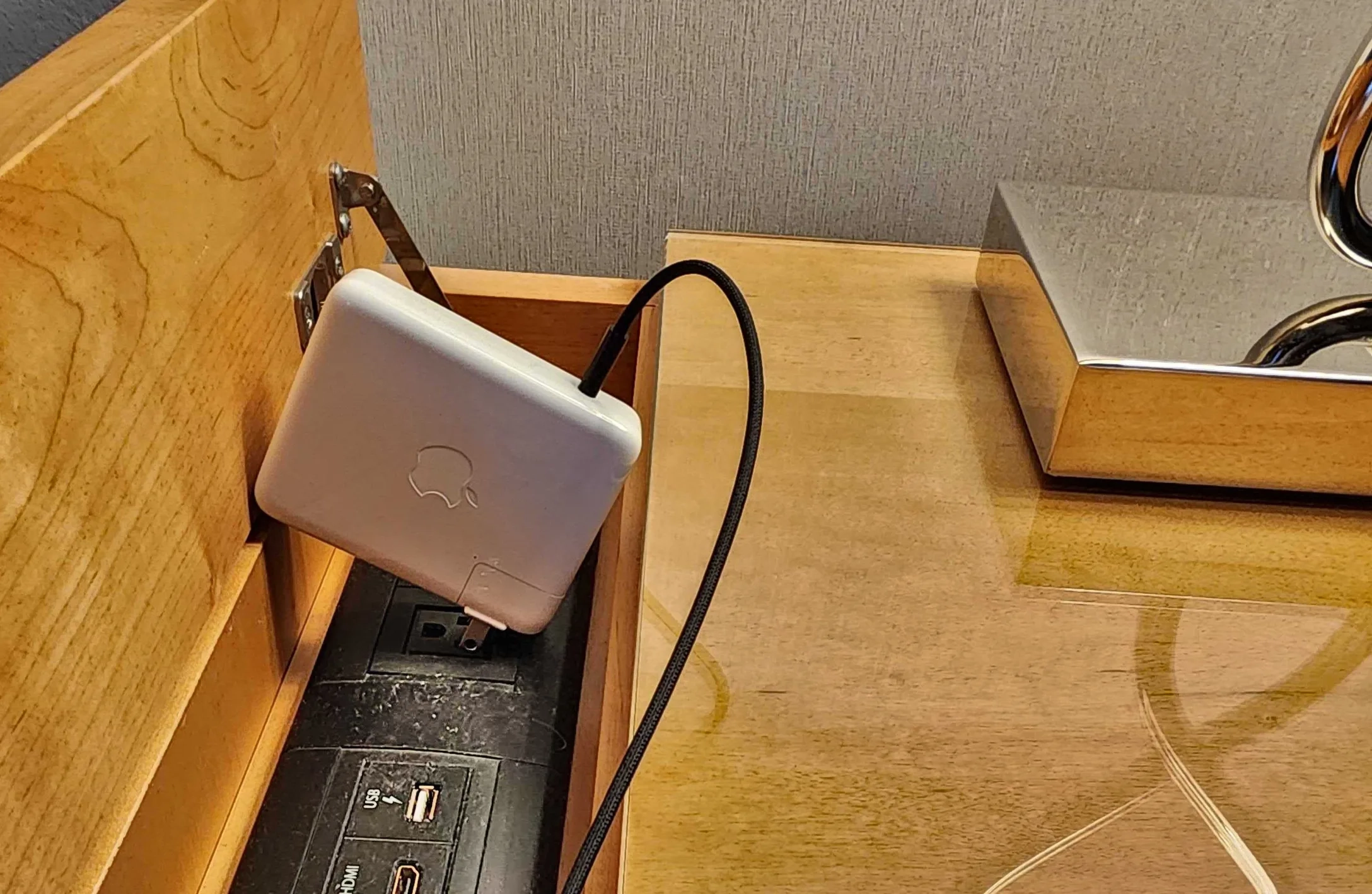 A hotel room desk: a laptop charger wedged into a power strip inside a wooden cabinet.